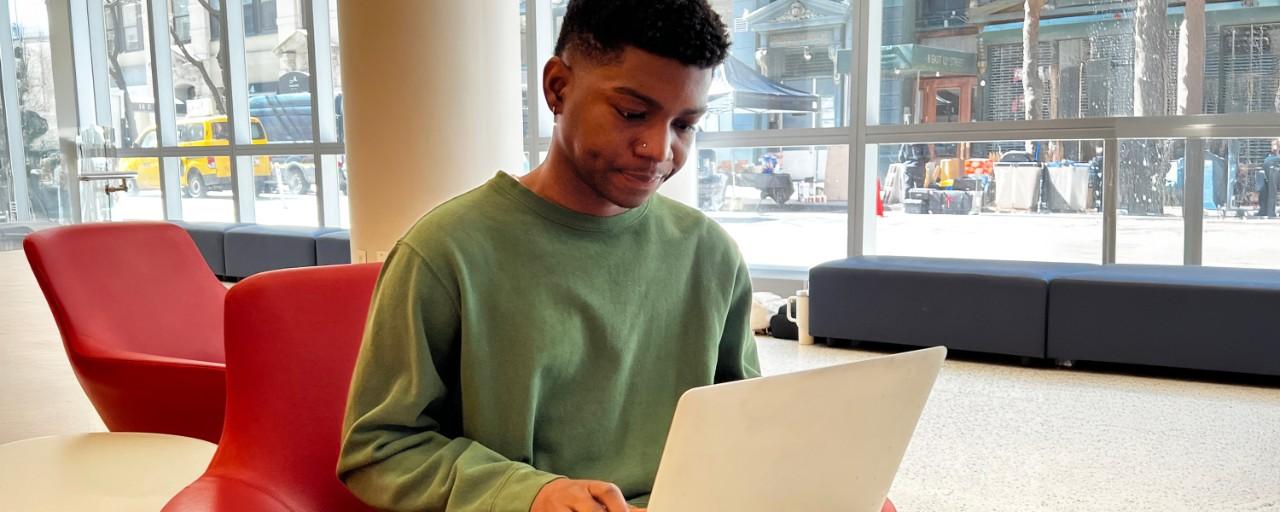 A male NYU student works at a computer in a spacious lounge.
