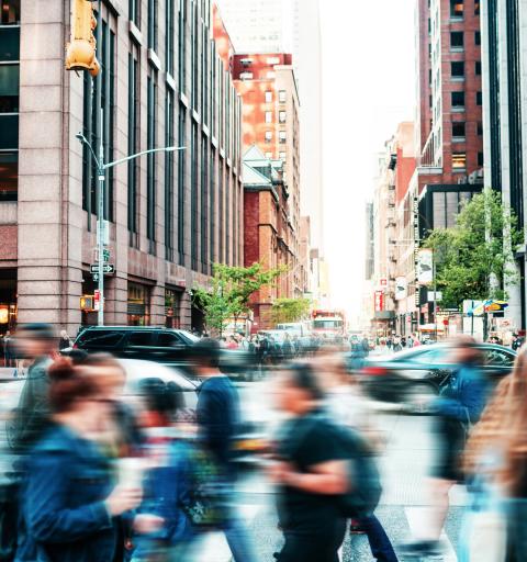 A blurred slice-of-life image containing pedestrians crossing a busy NYC intersection.