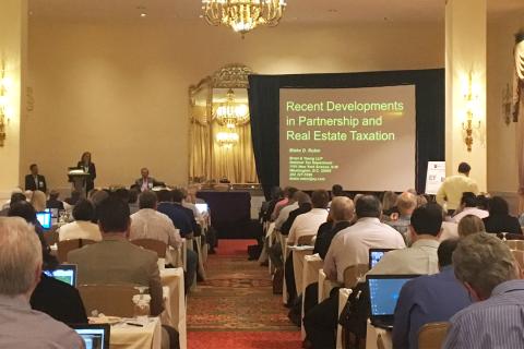 A guest speaker presents "Recent Developments in Partnership & Real Estate Taxation" to a ballroom at NYU SPS.