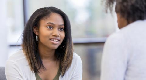 A woman leans in toward the camera to speak with a healthcare provider.