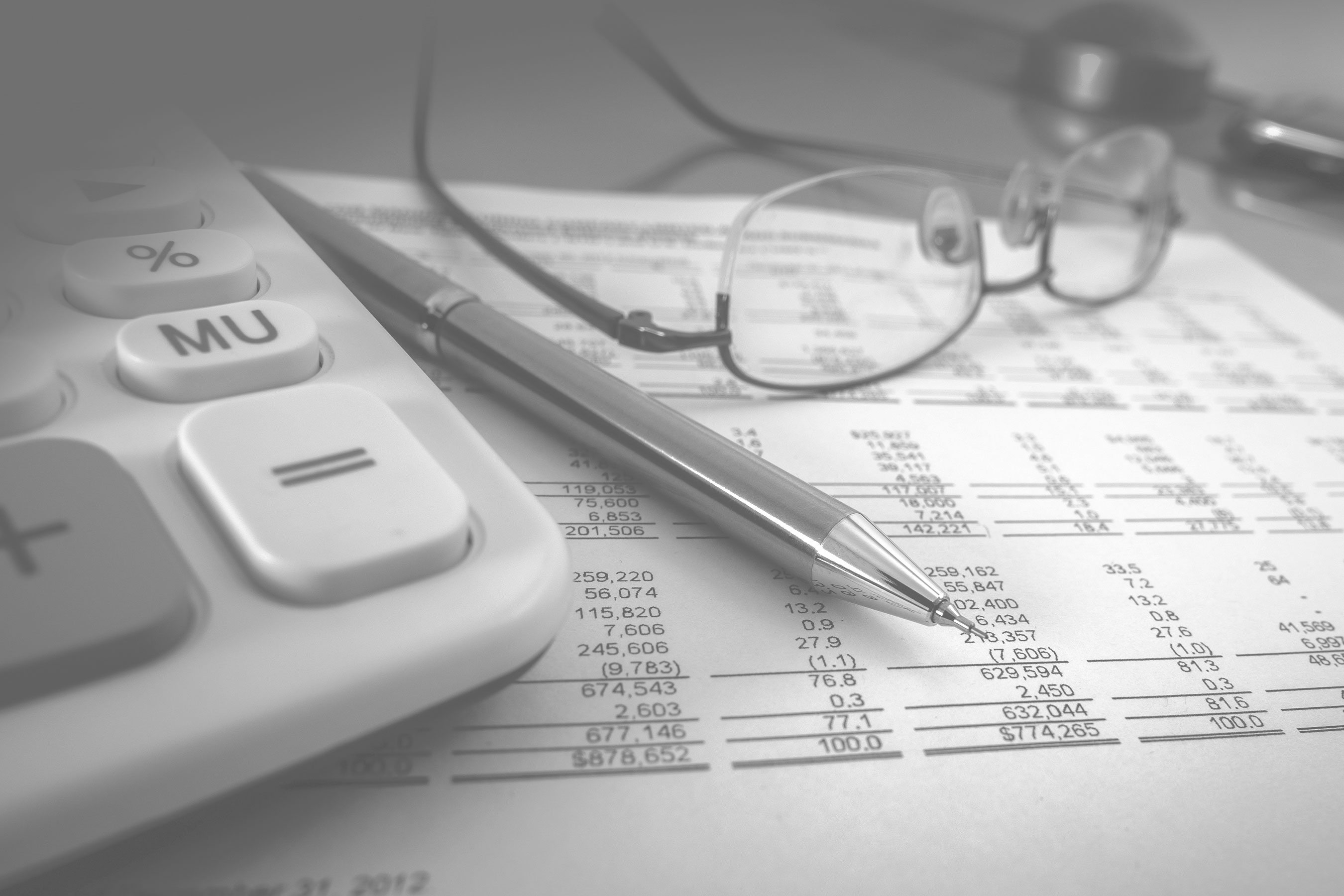 Glasses, a calculator, and a pen sit atop a printed spreadsheet.