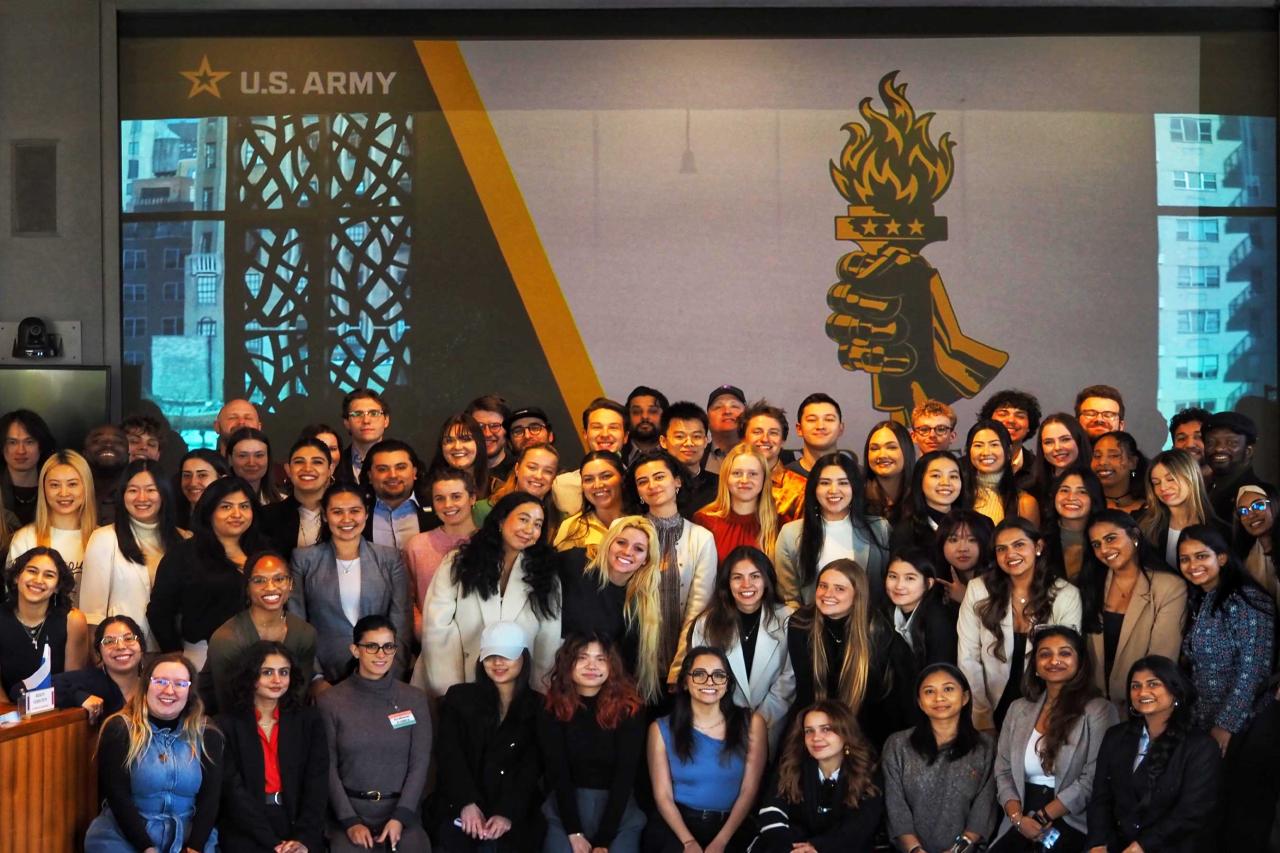 Group photo of diverse young adults in front of a US Army screen featuring a torch emblem.