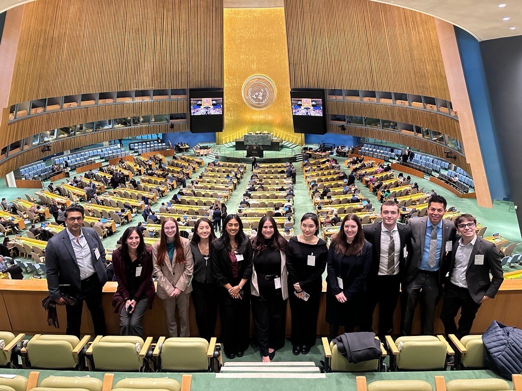 Students and faculty standing together inside the United Nations General Assembly Hall, overlooking the chamber and delegates seated below.