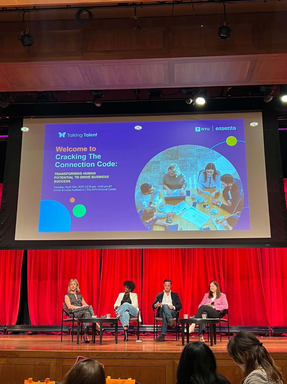 Panelists seated on stage during a discussion at the Cracking the Connection Code event, with the event title projected on a large screen behind them.