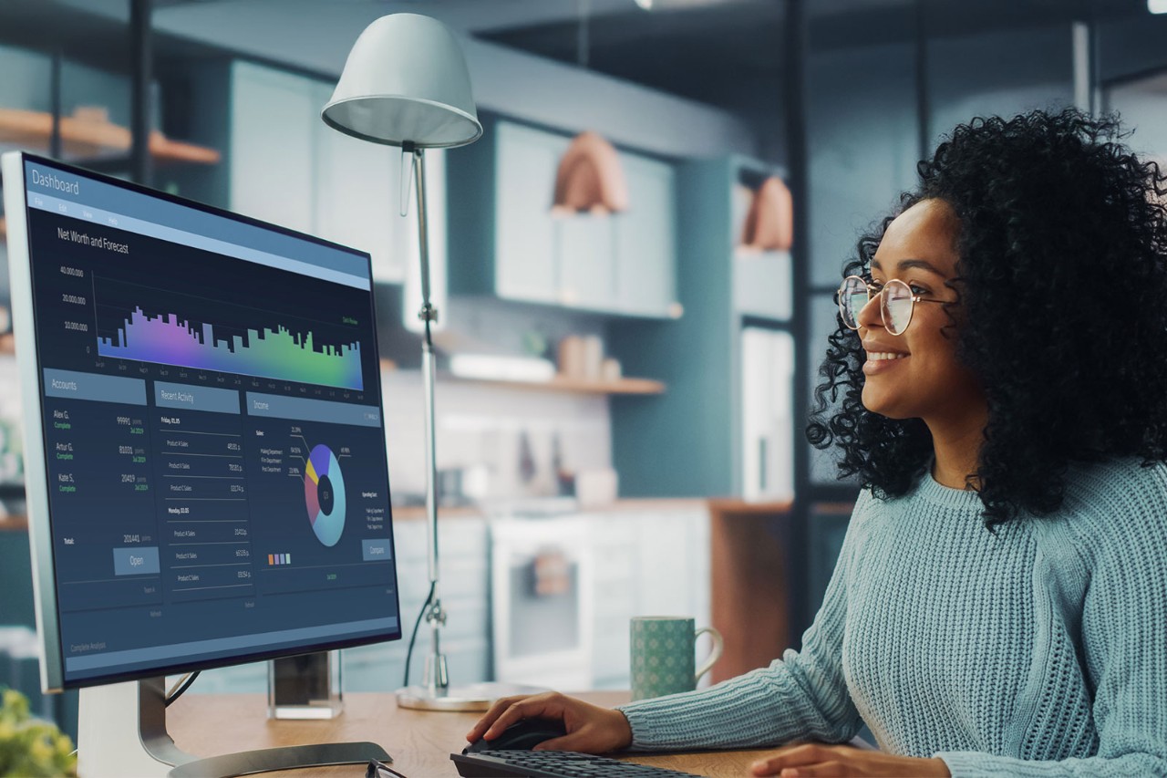 Person sitting at a desk smiling while working on a computer displaying data dashboards.