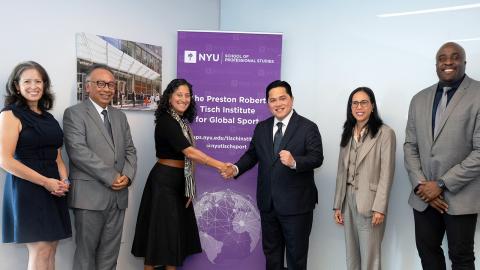 A group of six individuals in business attire shaking hands in front of an NYU SPS promotional banner.