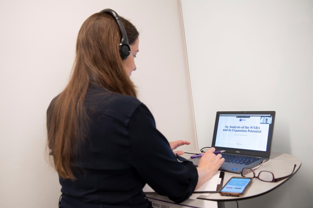 An NYU SPS student works on her capstone project titled "An Analysis of the WNBA and its Expansion Potential" on her laptop.