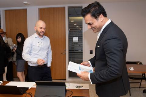A professionally dressed man jovially engages with a colleague while discussing paperwork in an office setting.