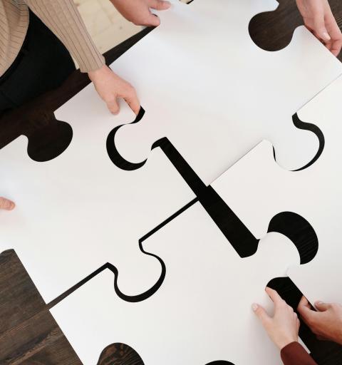 Four pairs of hands hold four large white puzzle pieces about to be fit together