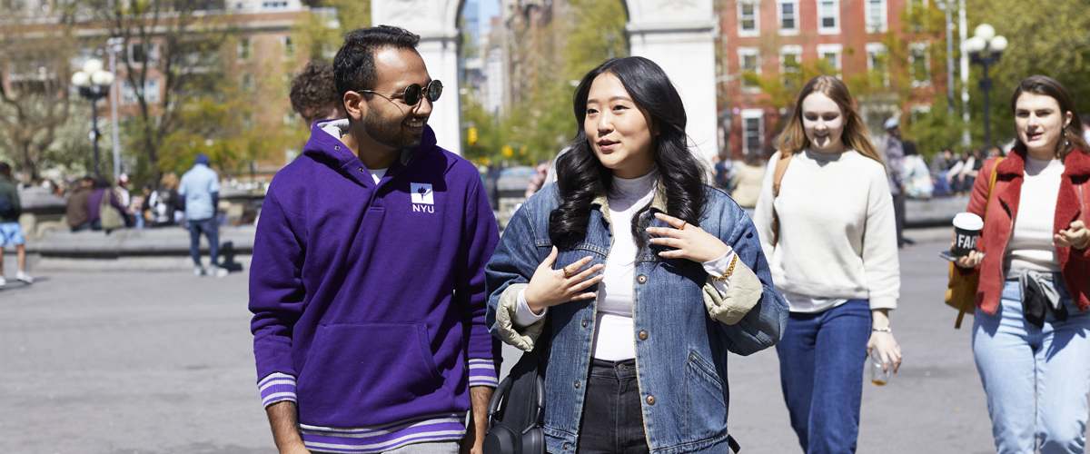 A pair of NYU SPS students walk through Washington Square Park on a bright sunndy day.