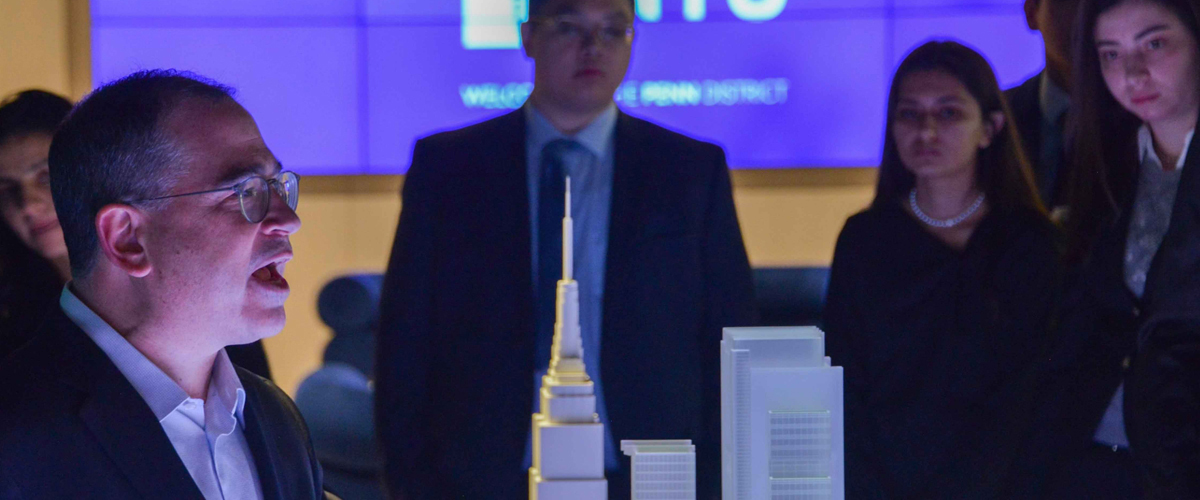 Participants at a Master's in Real Estate Development event gather around a building model to listen to a speaker