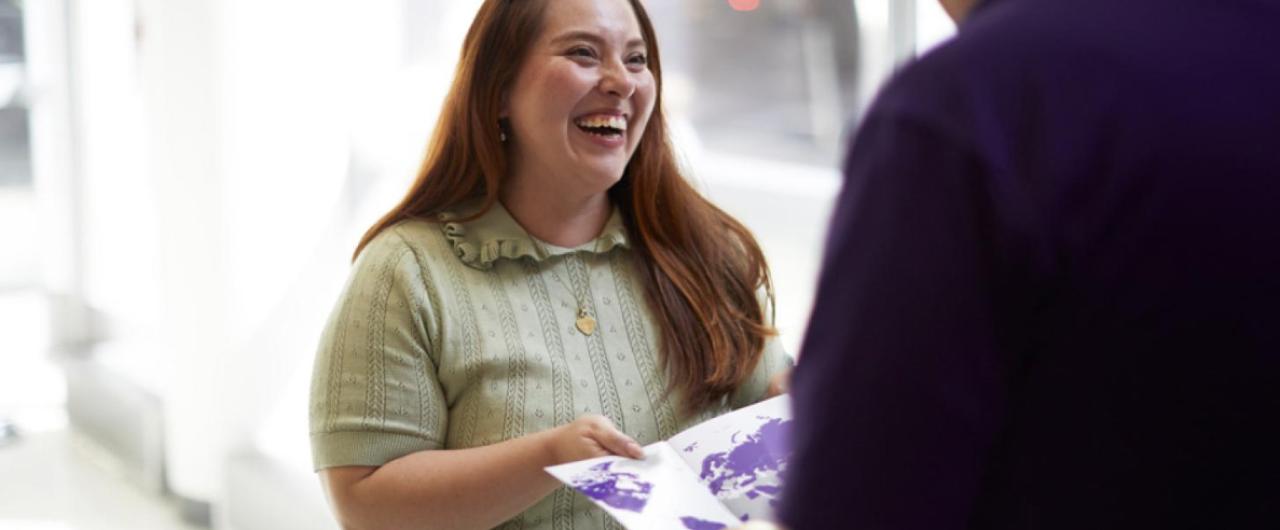 Smiling admissions officer hands holds pamplet in hands.