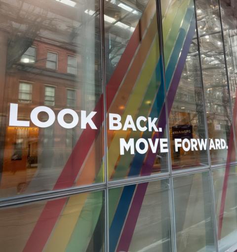 A window emblazened with a vinyl rainbow and the words "Look back. Move forward." in white vinyl lettering.
