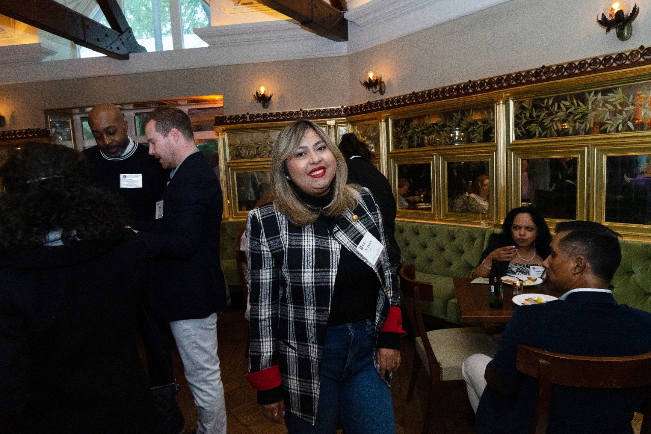 Bhavana Singh, Division of Programs in Business at NYU SPS alumnus, smiles for the camera in a crowded, dim dining room adorned with gold-framed portraits.