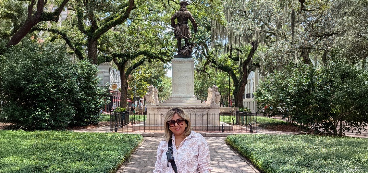 Bhavana Singh, Division of Programs in Business at NYU SPS alumnus, poses for a photo in front of a large bronze monument in a lush park.