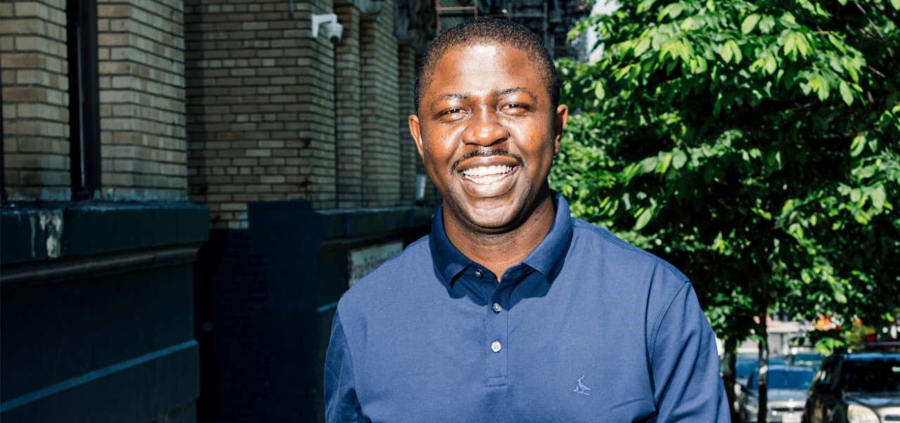 Edafe Okporo, NYU SPS Division of Programs in Business alumnus, smiles for the camera on a tree-lined New York City street.