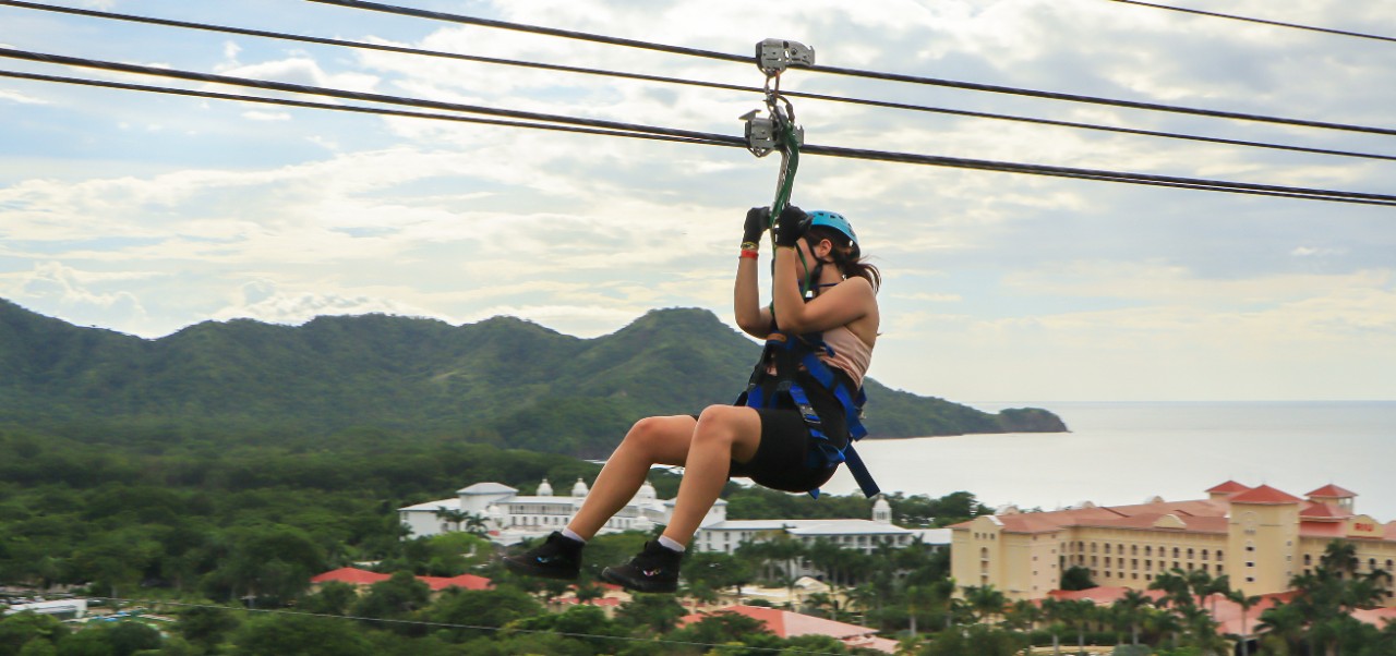Jessica Blodgett, NYU SPS Division of Programs in Business alumnus, zip lines along a coastal town with mountains and sea in the background.