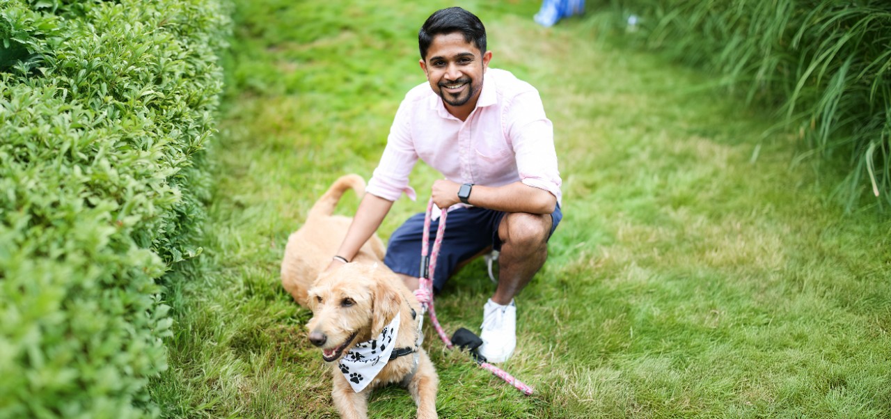 NYU SPS Division of Programs in Business alumnus Samarth Bedakihale poses for a photo with his golden retriever on a grassy clearing.