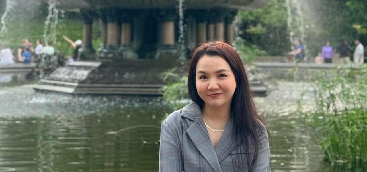 Siriluck Mim Rattanawaropas, NYU SPS Division of Programs in Business alumnus, smiles for the camera while sitting at a large fountain.