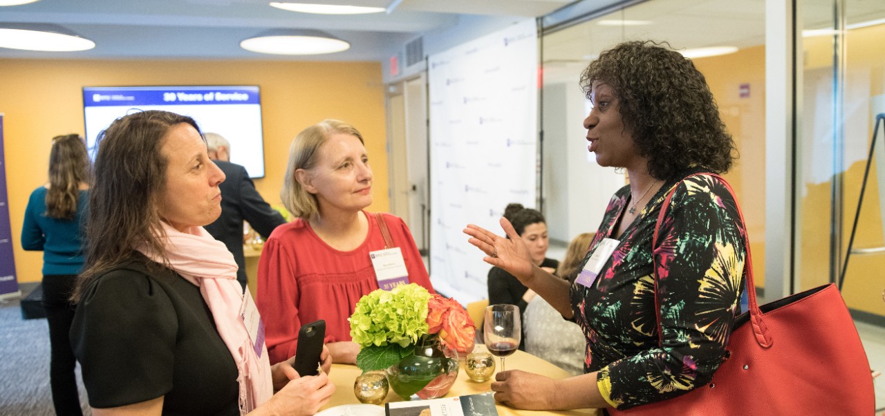 C. Belinda Levychin, Adjunct Instructor, Division of Applied Undergraduate Studies at NYU SPS networks with colleagues at a high-top table during a reception.