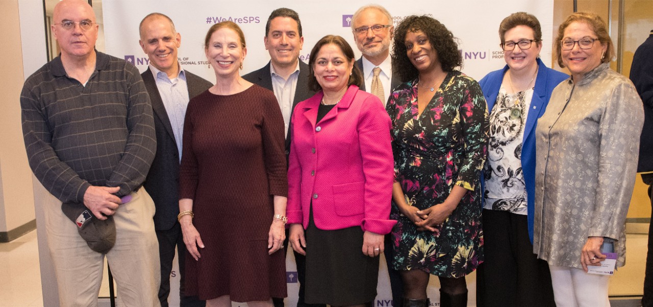 C. Belinda Levychin, Adjunct Instructor, Division of Applied Undergraduate Studies at NYU SPS poses for a photo with eight colleagues in front of a step-and-repeat.