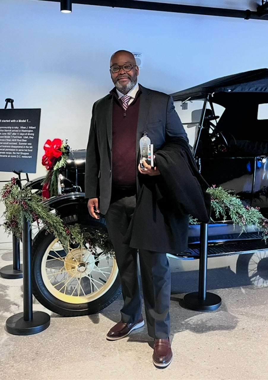 Brian C. Barker poses in front of a vintage automobile.