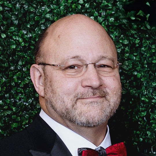 Charles Dorn poses for a photo at a holiday event at the University of Houston in front of a leafy background