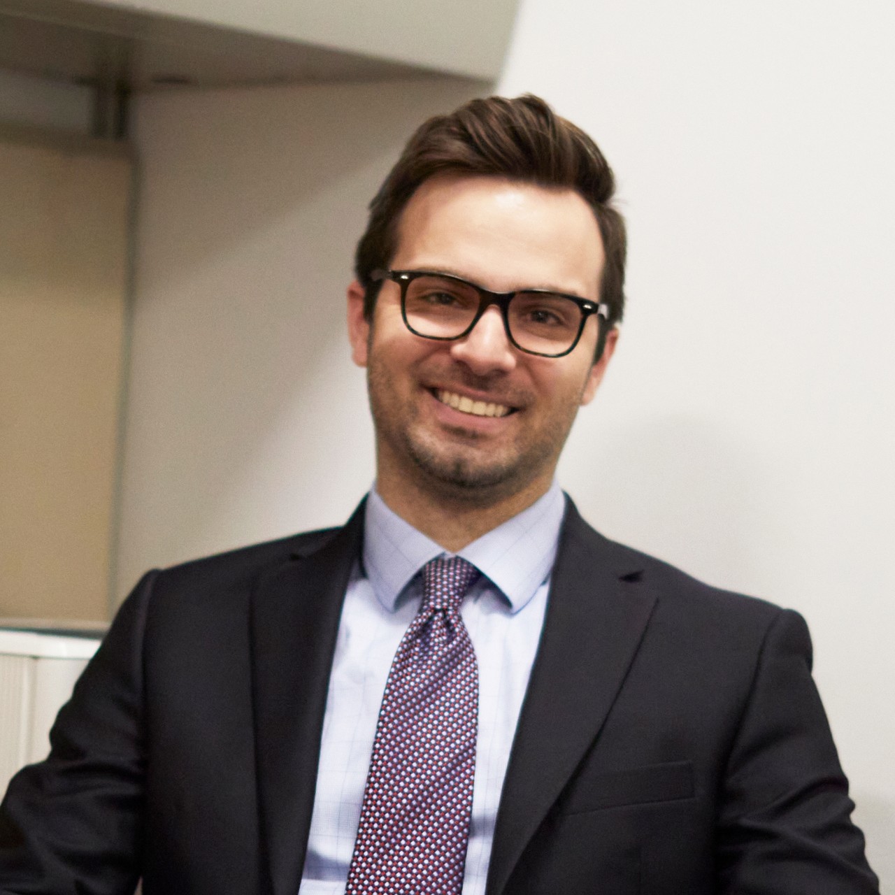 Colin Slabach sits with his hands folded in front of him for a headshot in an office setting