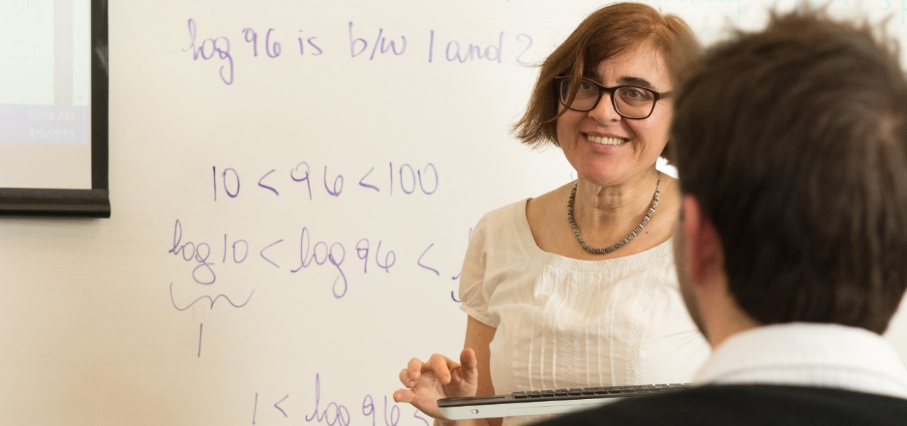 Donatella Delfino smiles while holding a keyboard and standing in front of a whiteboard with math concepts written on it