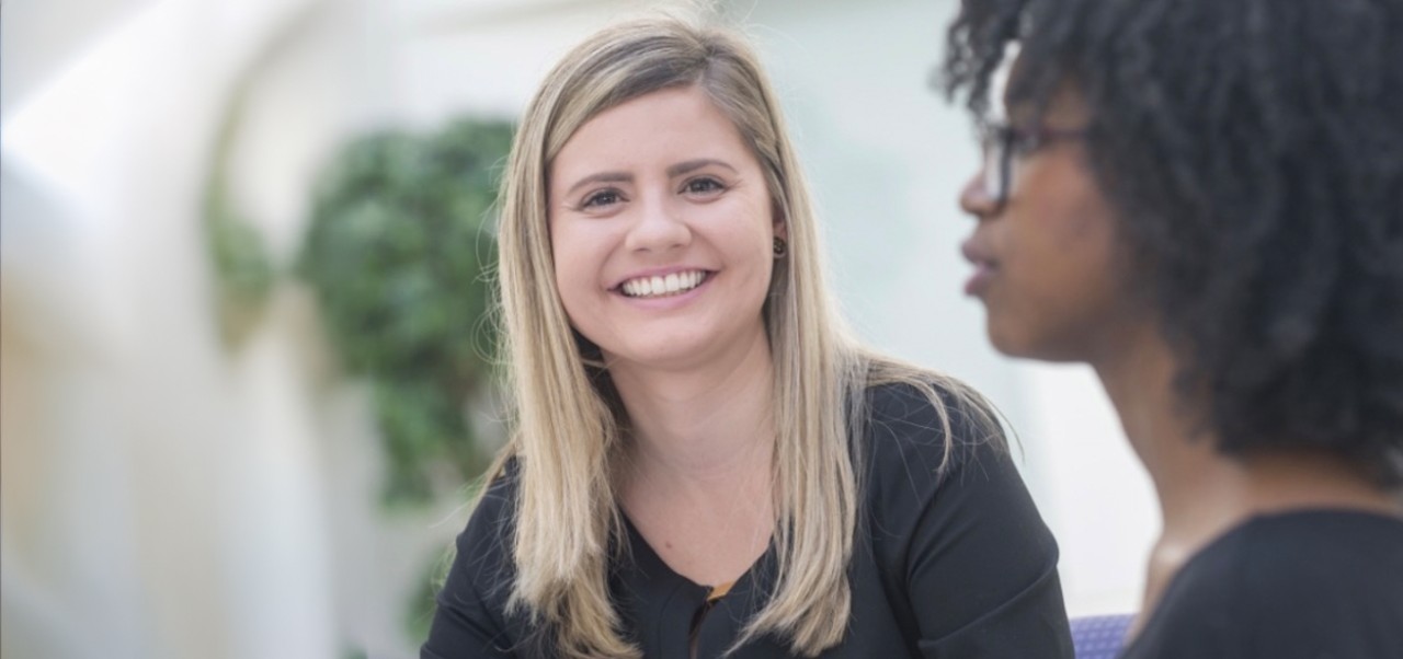 McKenna Schray smiles at the camera while sitting slightly behind someone who is out of focus and facing left