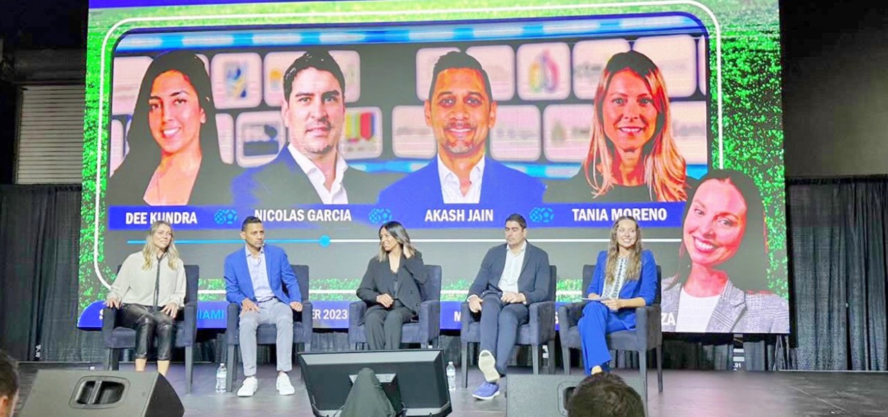 Sabrina Carrozza sits on the far right of a stage with four other people at Soccerex Miami