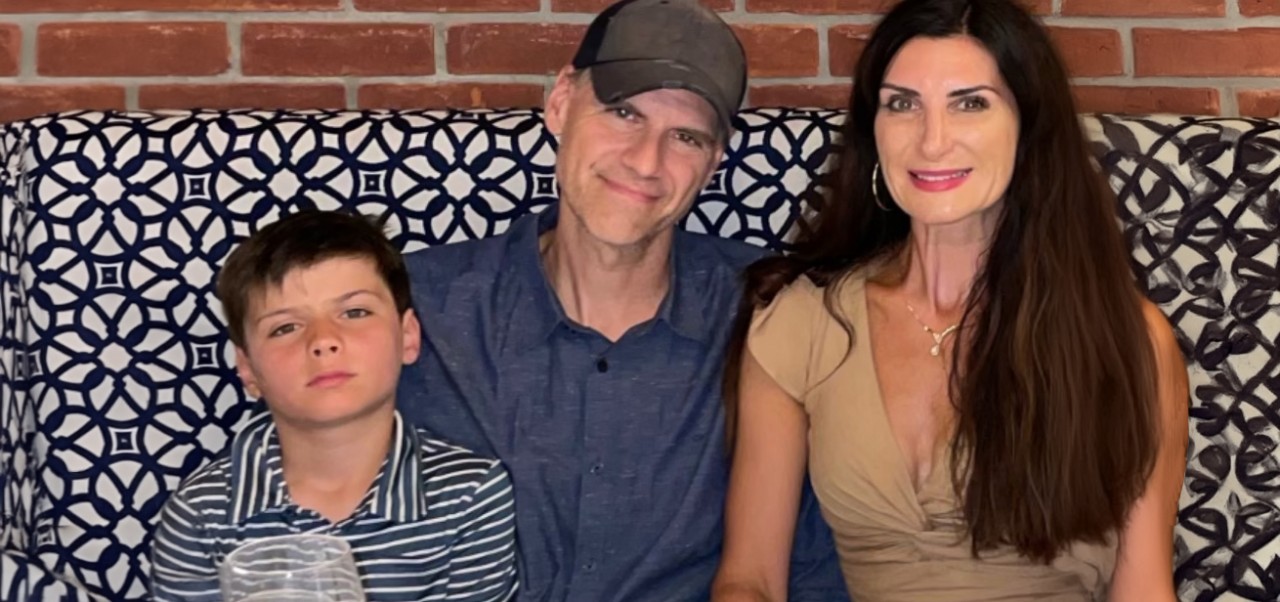 Dr. Steven Goss,  Clinical faculty member and chair of the Management and Technology program in the Division of Programs in Business at NYU SPS, poses for a photo with his wife and son while seated at a bench.