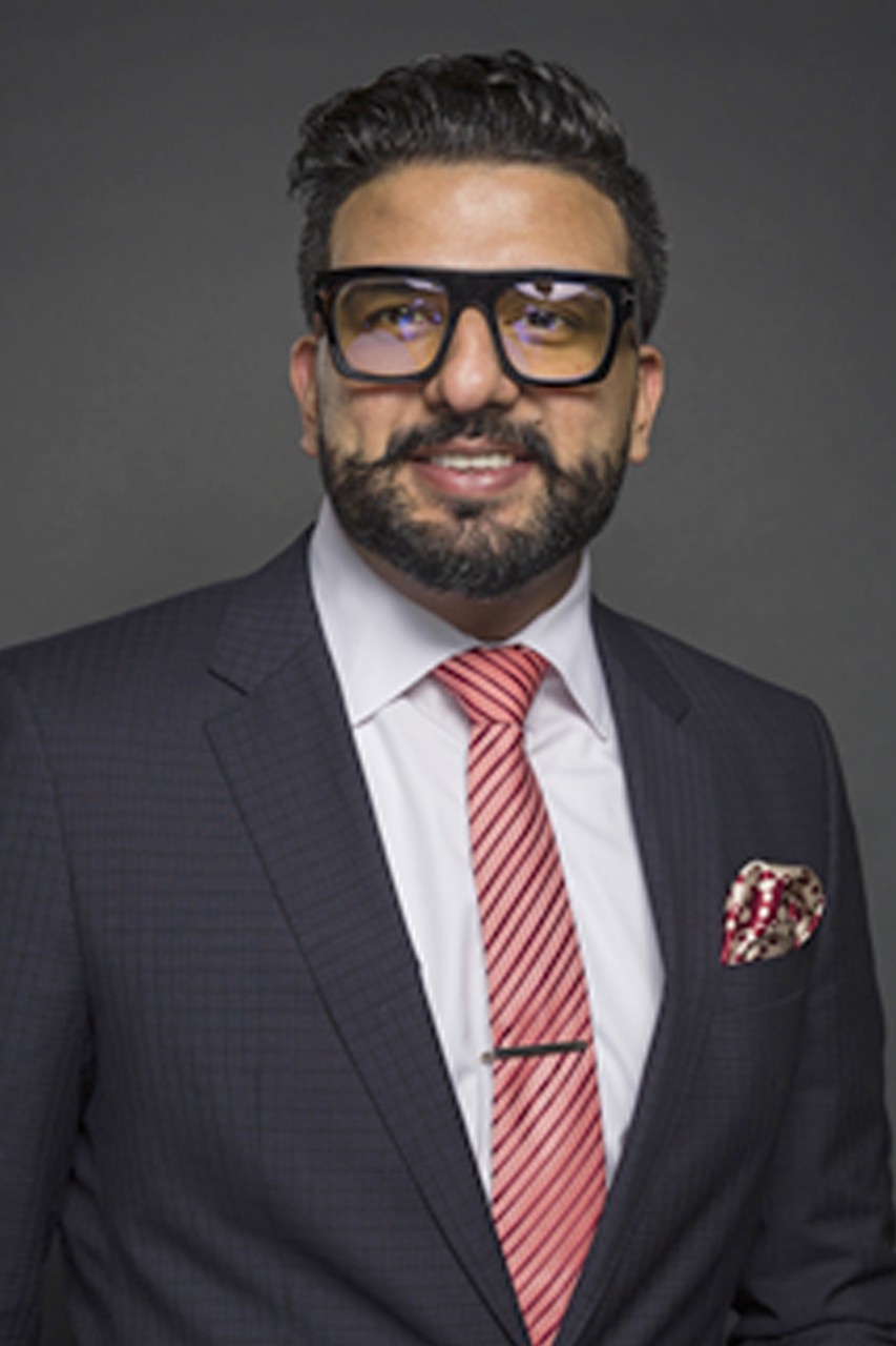 Zair Cheema poses for a headshot wearing a navy suit in front of a grey background