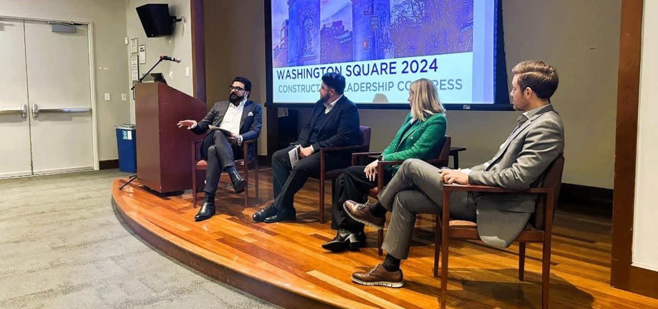 Four people sit on a stage at the Washington Square 2024 Construction Leadership Congress and Zair Cheema (far left) is speaking to a crowd that is out of view.