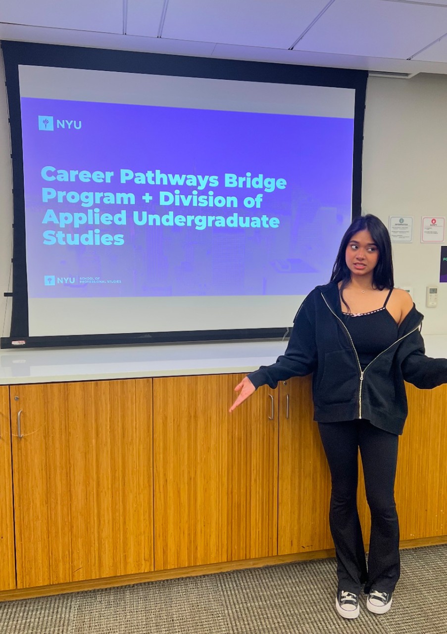Fathima Ballee stands gesturing towards a projection screen displaying NYU's Career Pathways Bridge Program slide.
