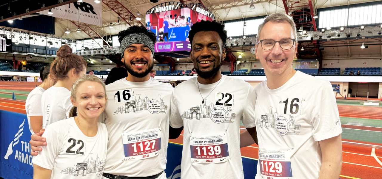 Joshua Murray, Division of Programs in Business student at NYU SPS, poses for a photo with three fellow runners during a marathon at an indoor track