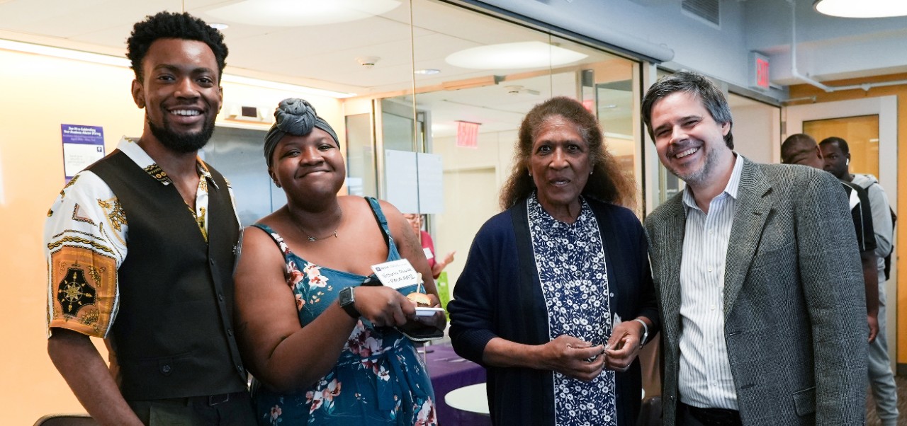 Joshua Murray, Division of Programs in Business student at NYU SPS, poses for a standing photo alongside three colleagues in an office building hallway.