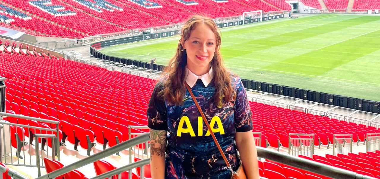 Morgan Baker, student at the NYU SPS Preston Robert Tisch Institute for Global Sport, poses for a photo in a massive, empty football arena.