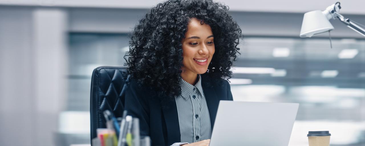 A woman works at a laptop computer while seated at a desk in a modern office.