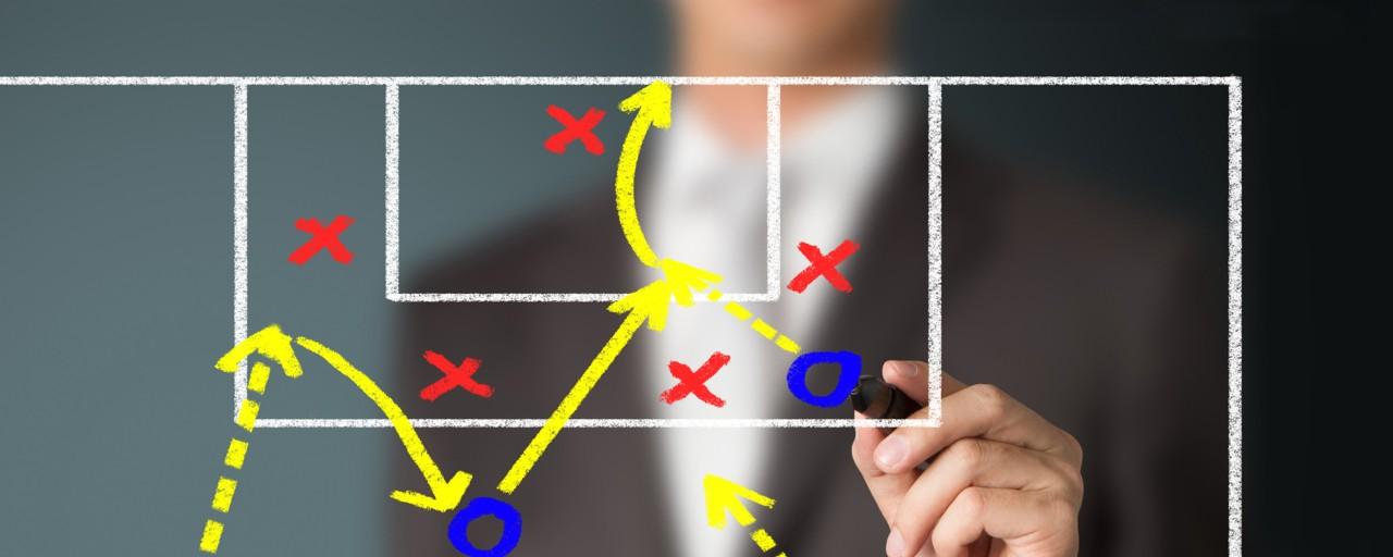 Demonstrating coursework in the Certificate in Sports Analytics program, a person in the background draws a basketball play on a digital display in the foreground.