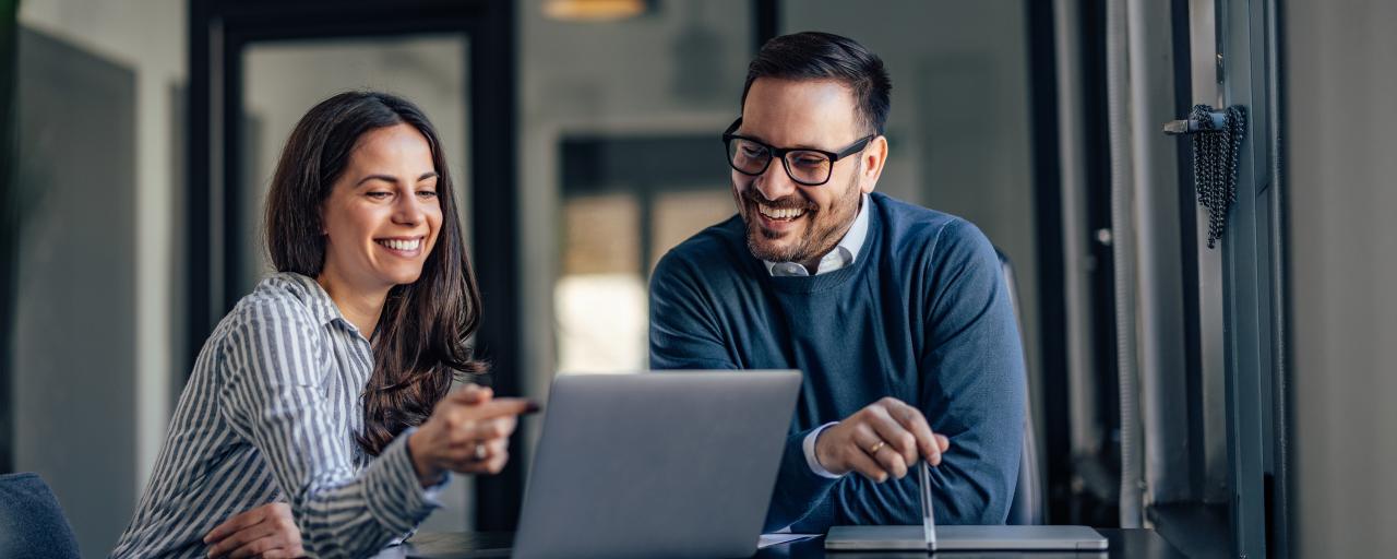 Two colleagues discuss work over a laptop computer in an office.