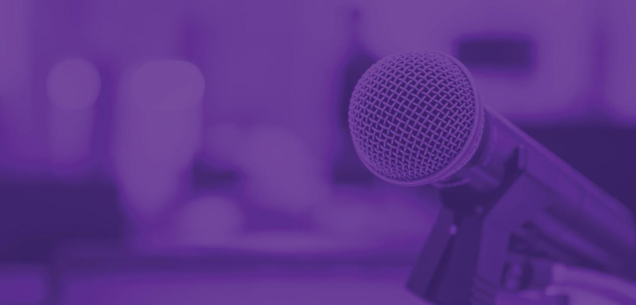A woman draws on a transparent white board while demonstrating a business concept to colleagues seated at a table in the background.