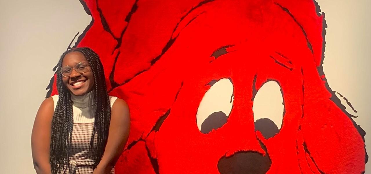 Abigail Jordan, Center for Publishing and Liberal Arts at NYU SPS alumnus, poses for a photo in front of a mural featuring Clifford the Big Red Dog.