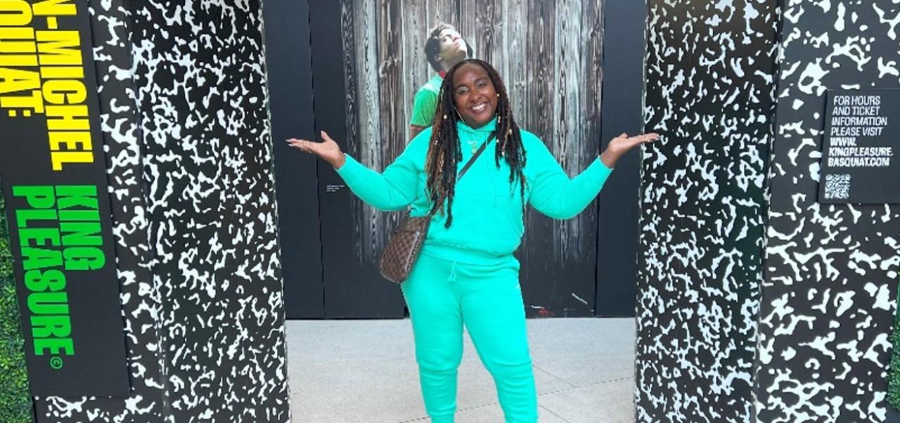BA in Social Sciences alum Shakia Rose poses in front of a Jean-Michel Basquiat King Pleasure art installation