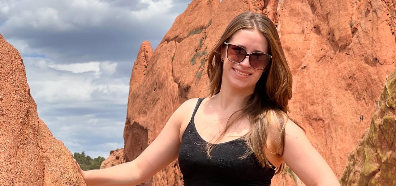 Talia Barrington, NYU SPS Division of Applied Undergraduate Studies alumnus, smiles for the camera amidst dramatic red boulders.