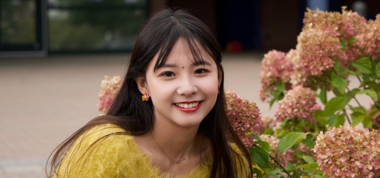 Yi Li, Division of Programs in Business at NYU SPS alumnus, poses for a photo in front of pink hydrangeas.