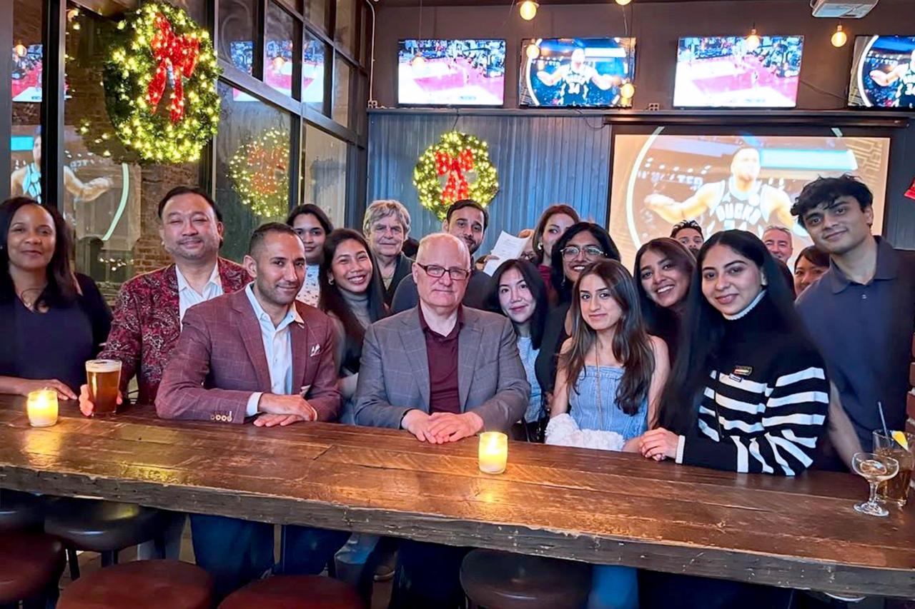 Lawrence Mantrone, faculty member in the Continuing Education programs at NYU SPS sits at a table in a restaurant surrounded by certificate program students
