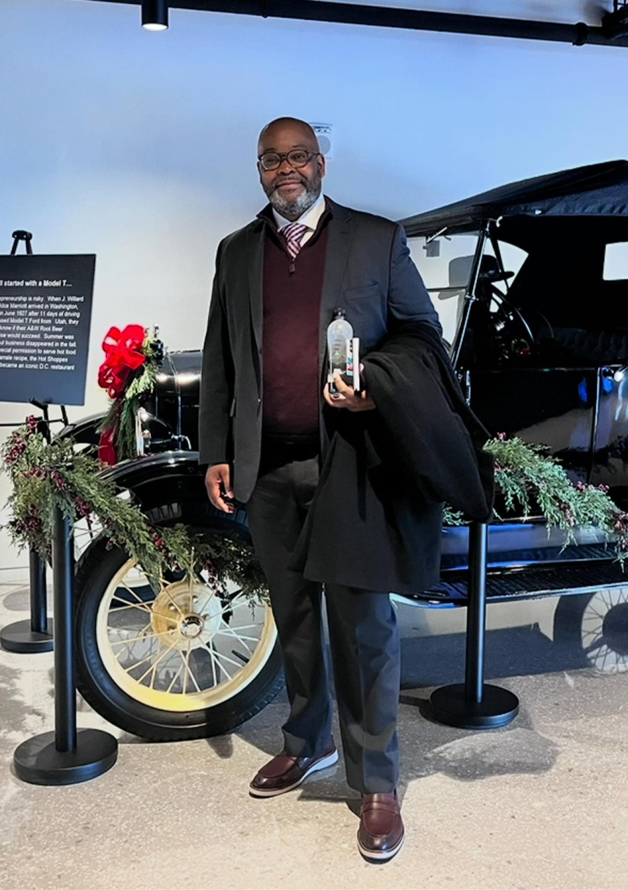 Brian C. Barker poses in front of a vintage automobile.