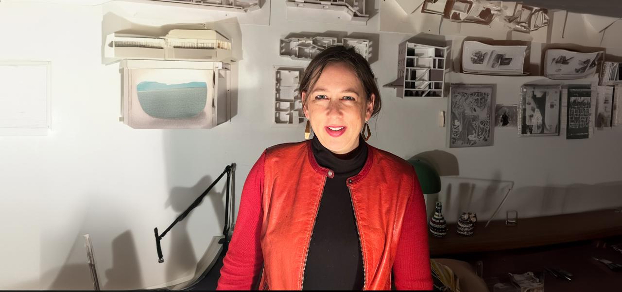 Julie Torres Moskovitz wears a red jacket while standing in front of architectural models in her home office in Brooklyn.