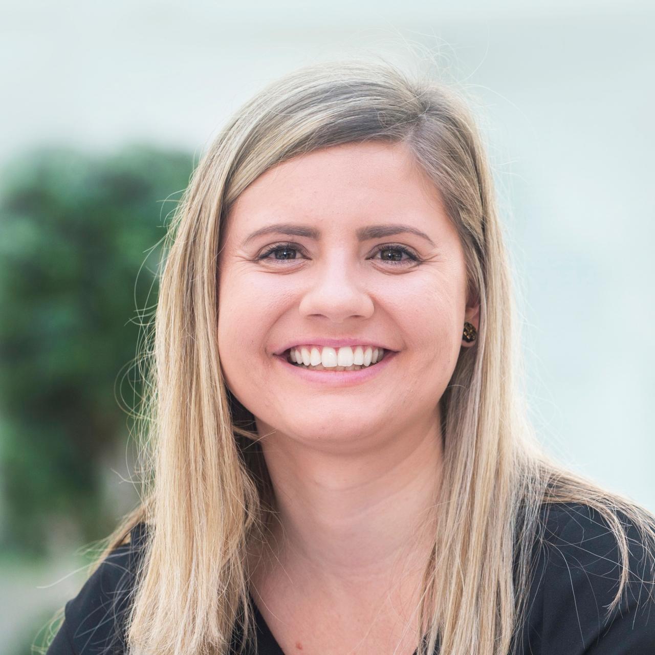 McKenna Schray smiles for a headshot while wearing a black long sleeve shirt with a white and green background